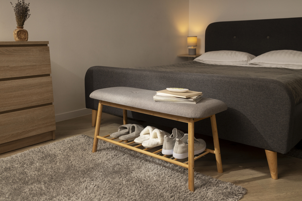 Dormitorio decorado con una banqueta de madera y tapizado gris al pie de la cama, ideal para guardar zapatos y añadir funcionalidad al espacio.